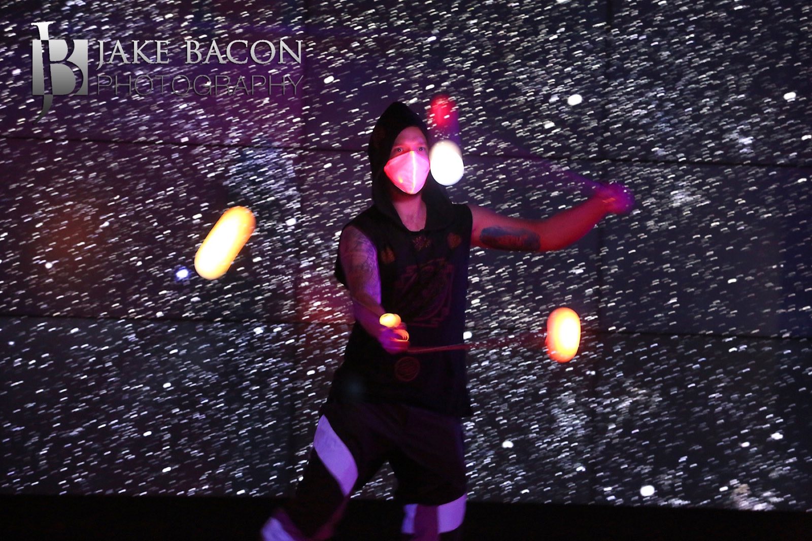 Black-clad performer juggling illuminated clubs against a field of static