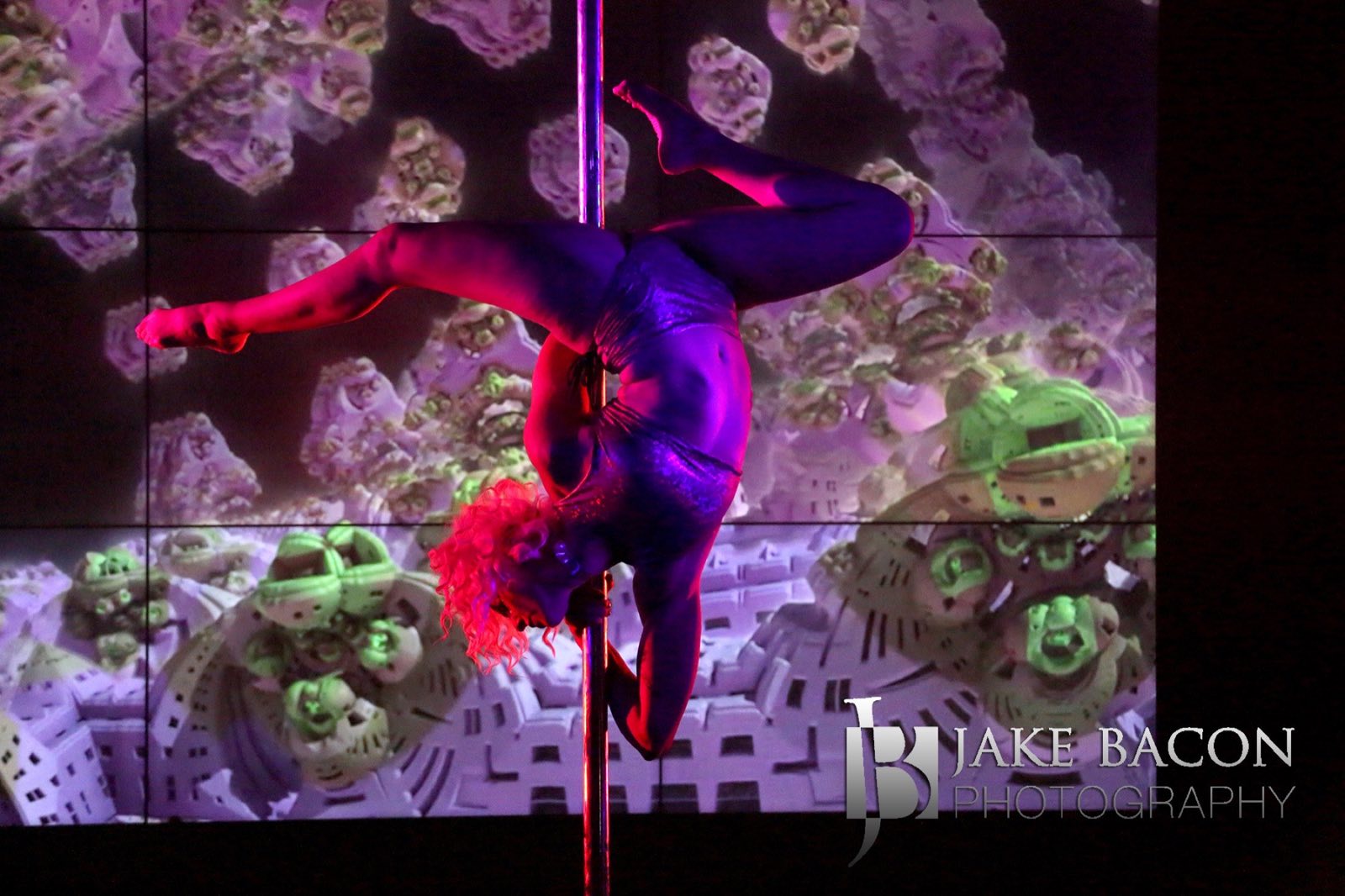 Pole artist suspended upside down before a colorful projected collage