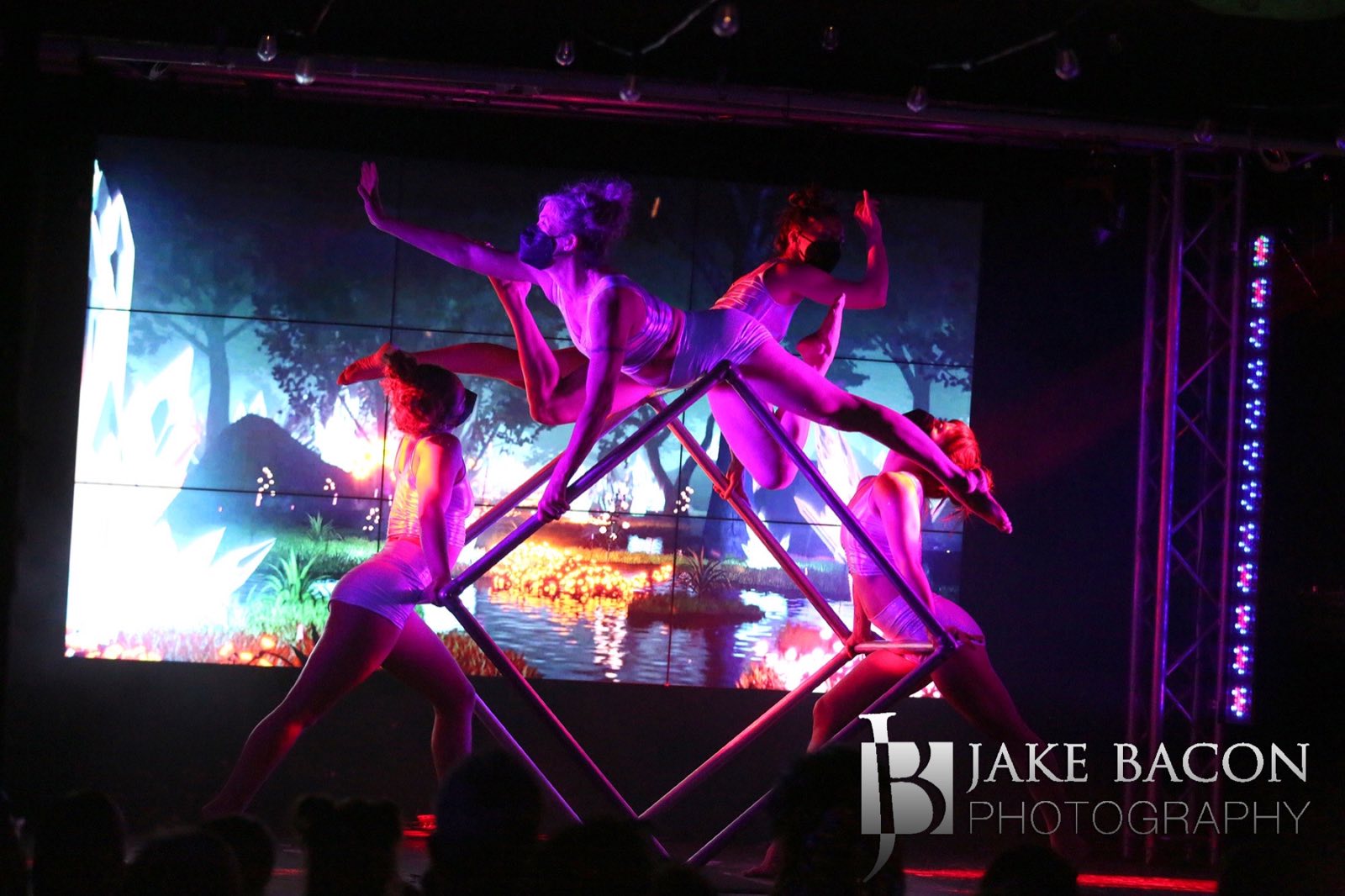 Four aerialists balancing together on a suspended metal cube