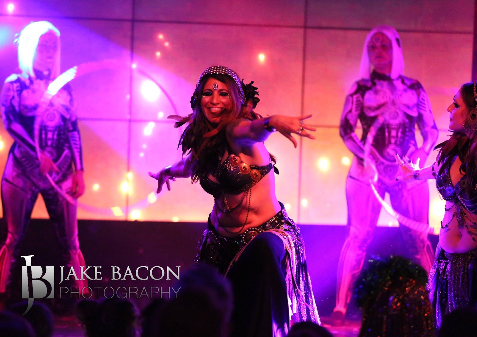 Belly dancer reaching toward the audience with silver robot characters behind her