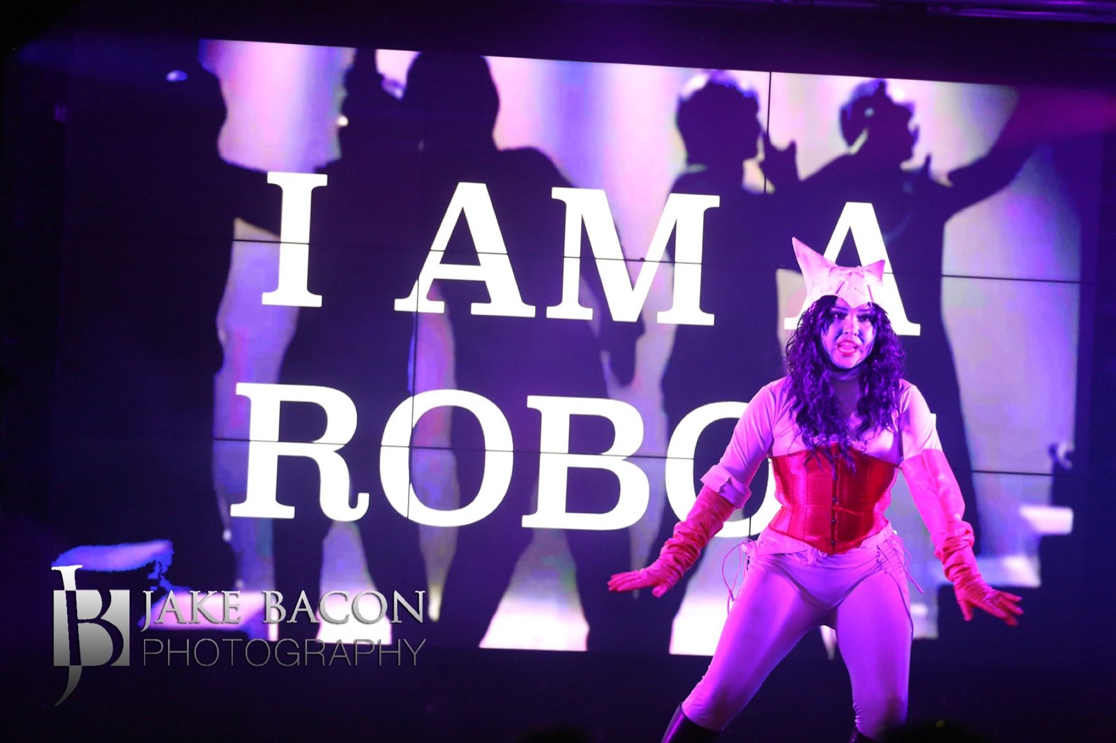 Dancer posing beneath projected words declaring I am a robot