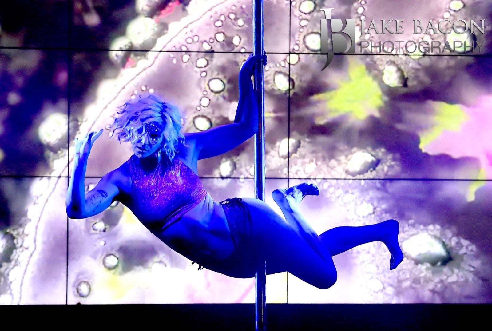 Aerial performer extending horizontally across a hoop before a cosmic projection