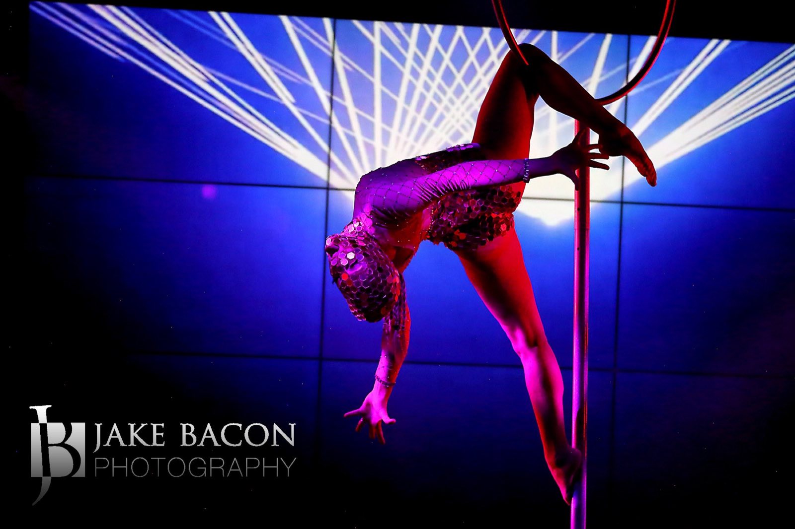 Pole performer holding an inverted split in red and blue stage light