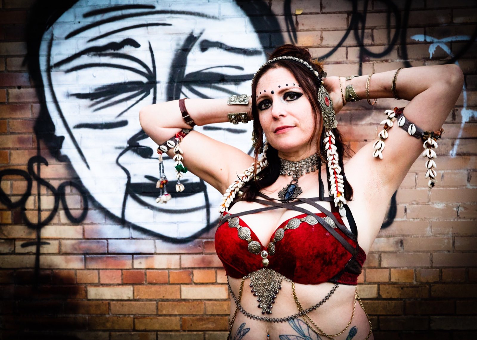 Red-costumed belly dancer posing with her arms behind her head
