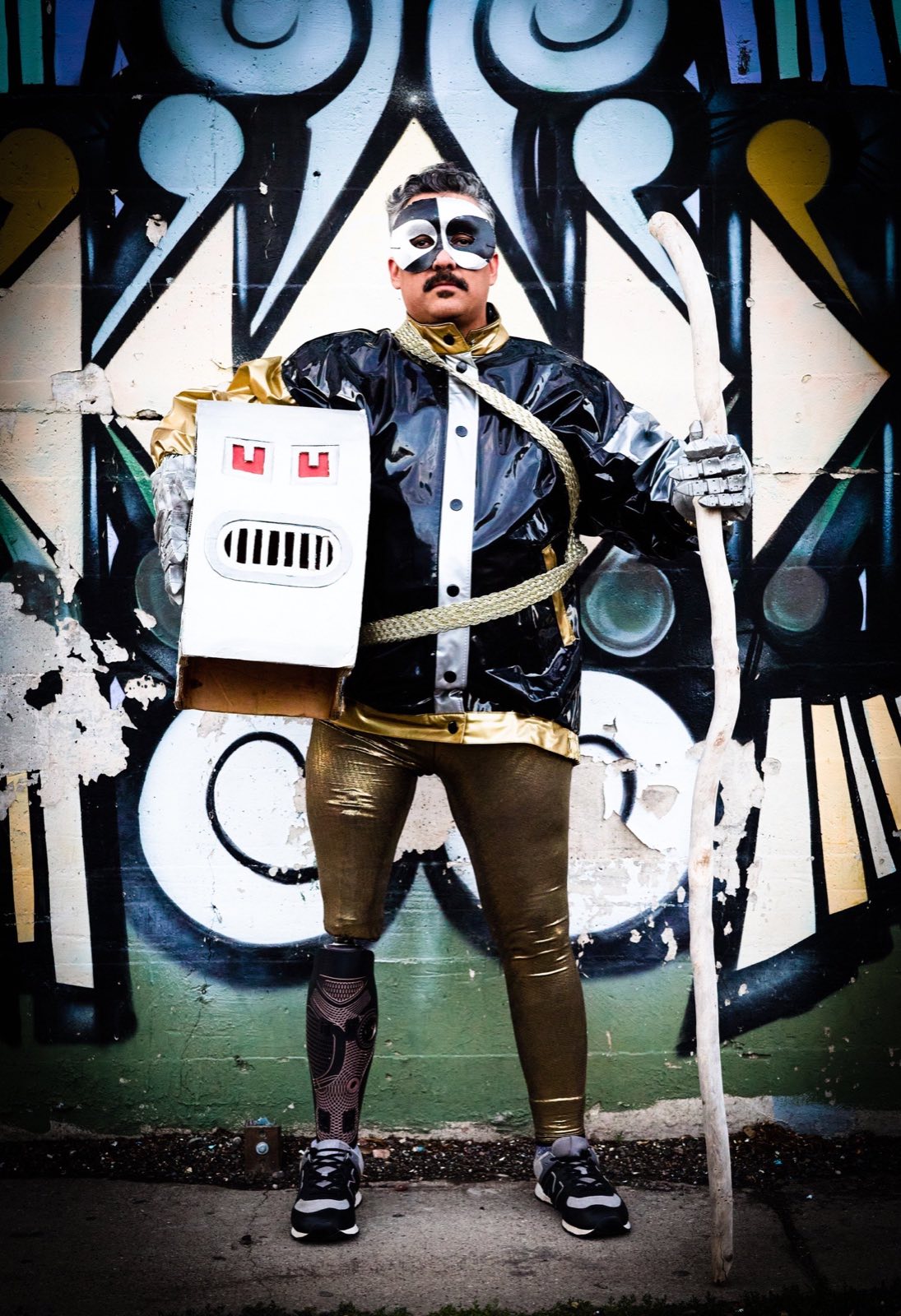 Box-headed robot character standing with a cane before black-and-white graffiti