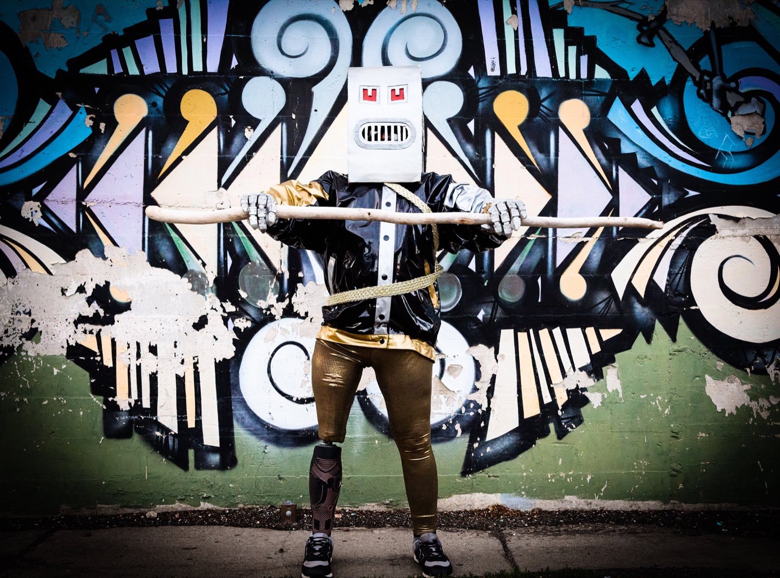 Box-headed robot extending both mechanical arms across the alley mural