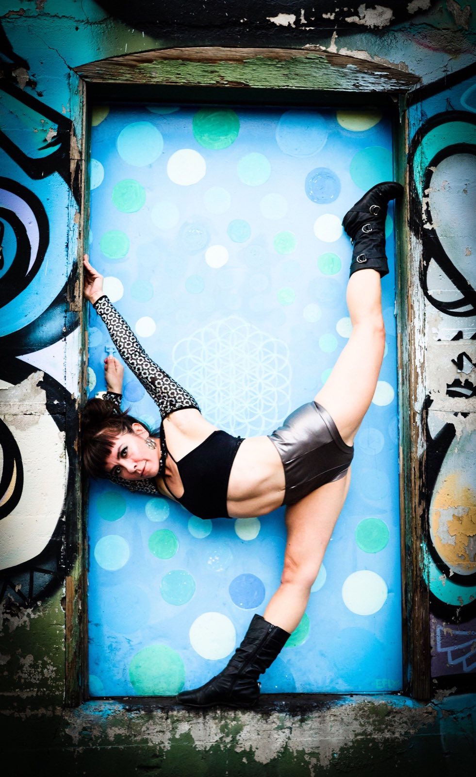 Silver-costumed performer holding a wide inverted pose in a blue doorway