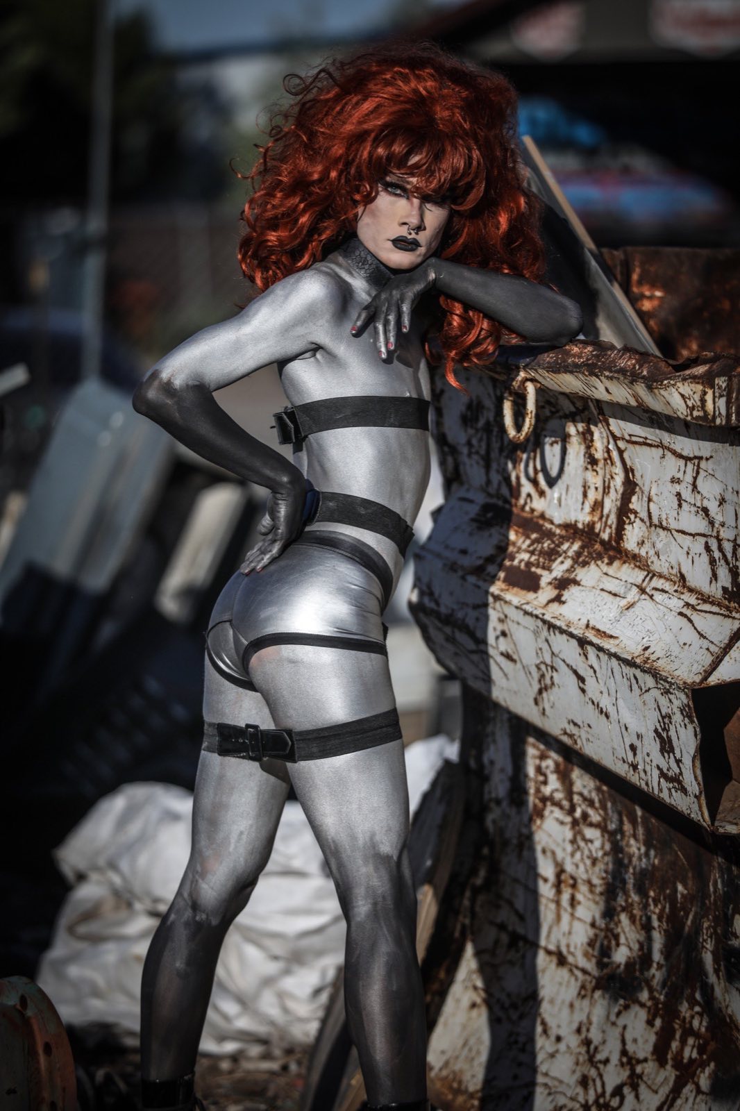Red-haired silver robot character crouching beside rusted machinery