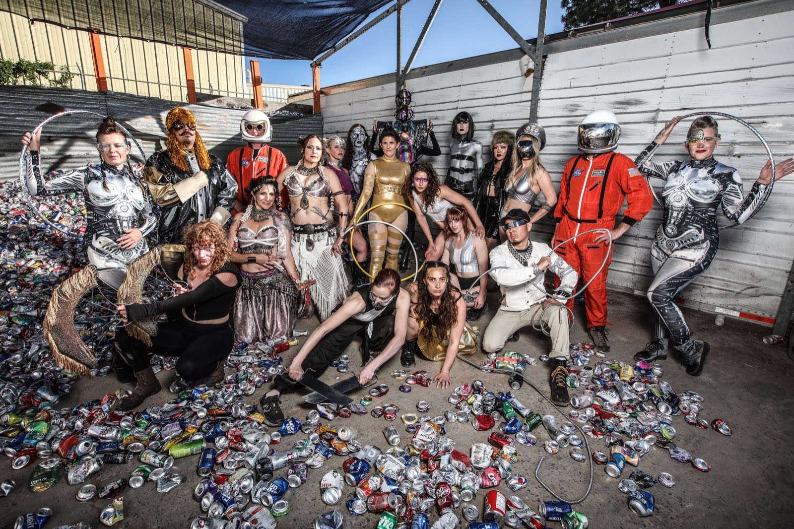 Large 2023 character ensemble posing amid piles of crushed aluminum cans