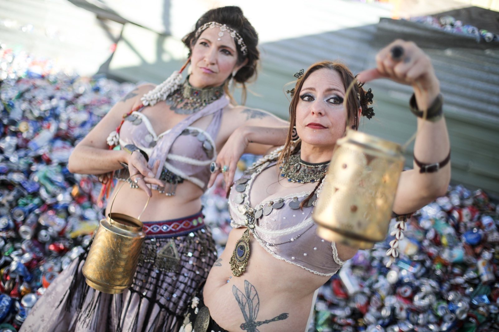 Two metallic-costumed performers posing together above a mound of cans