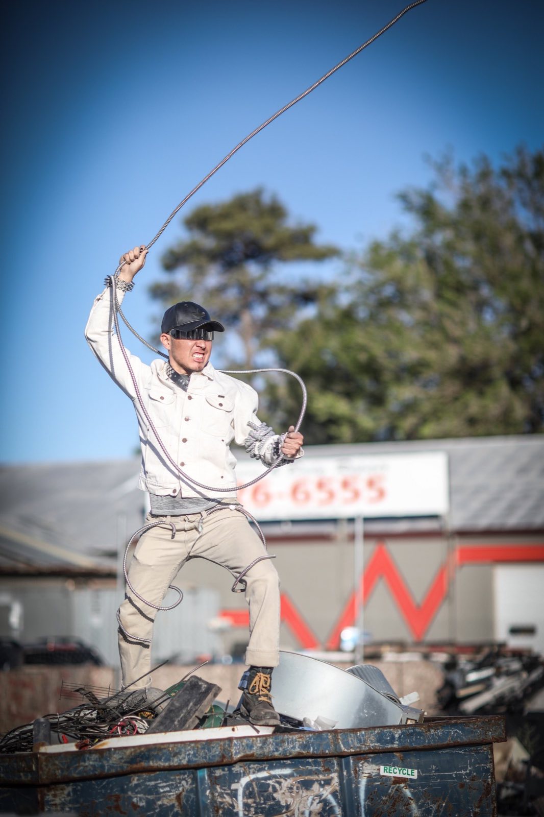 White-costumed performer raising one hand against the open junkyard sky