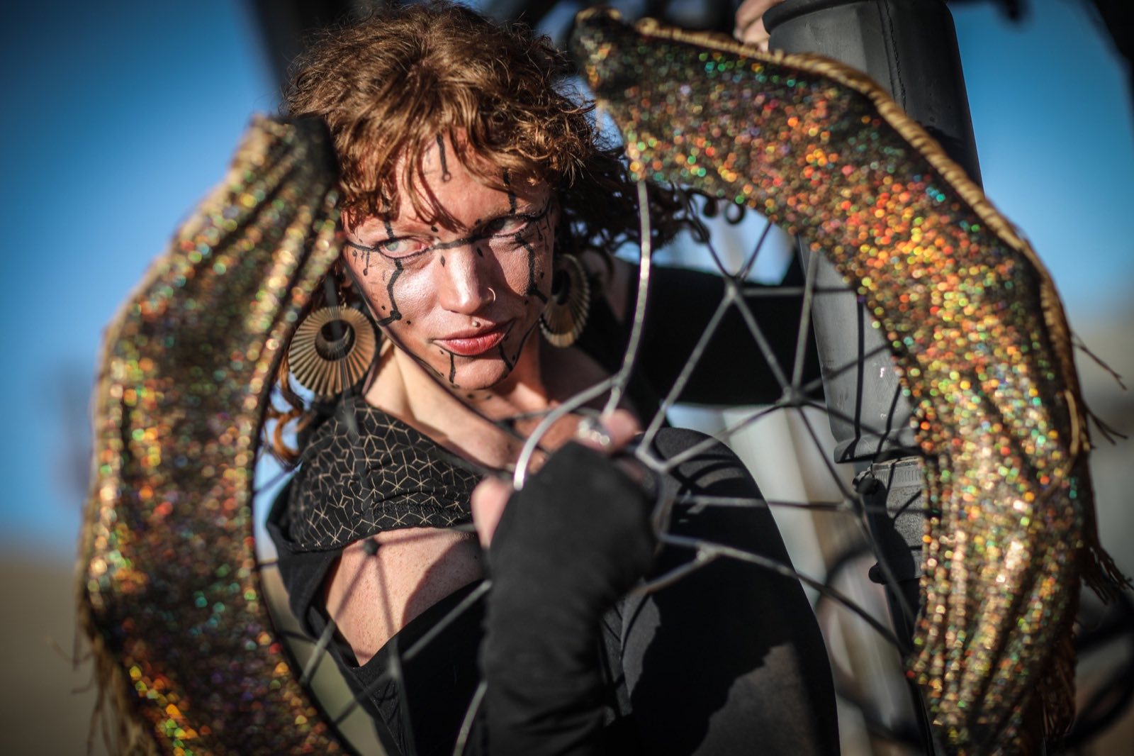Curly-haired performer framed inside a round metallic prop