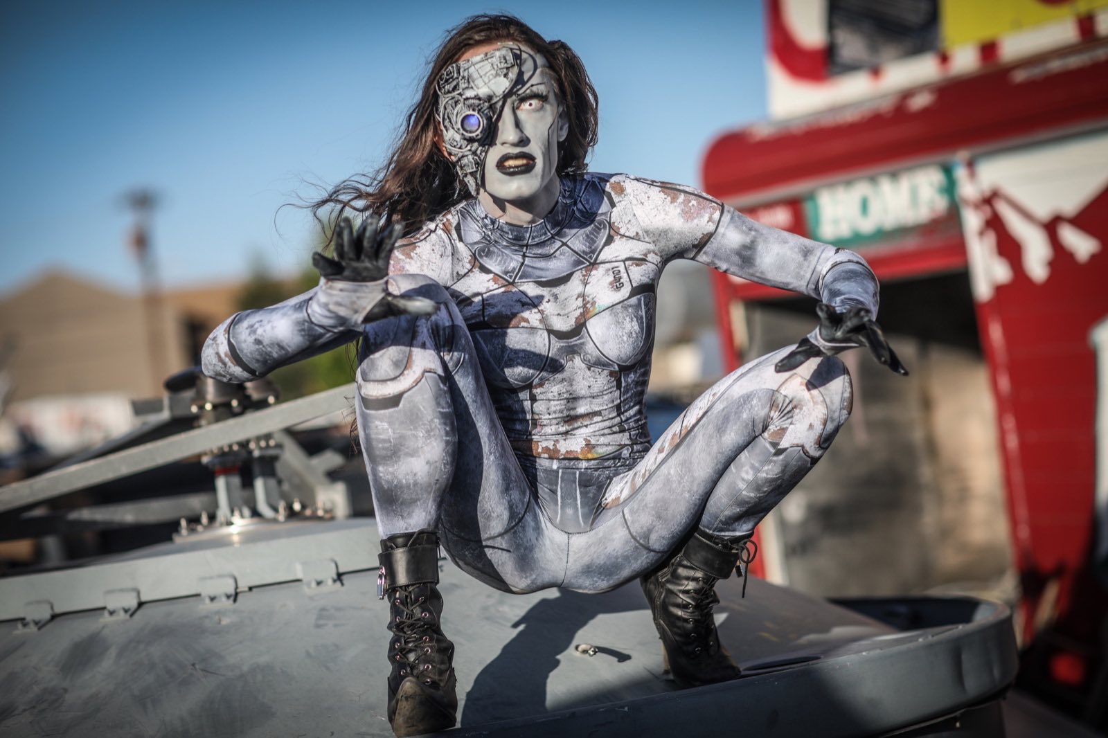 Silver-painted robot character seated on discarded industrial equipment