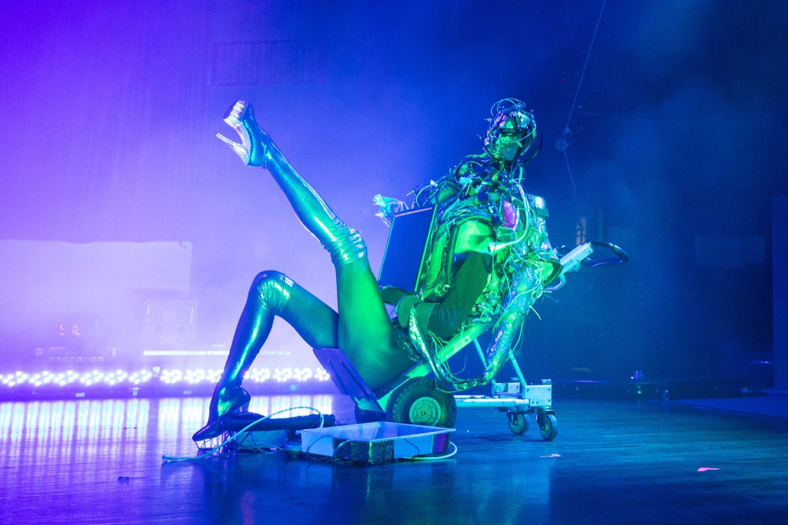 Green-lit performer seated beside a towering wire-covered robot character