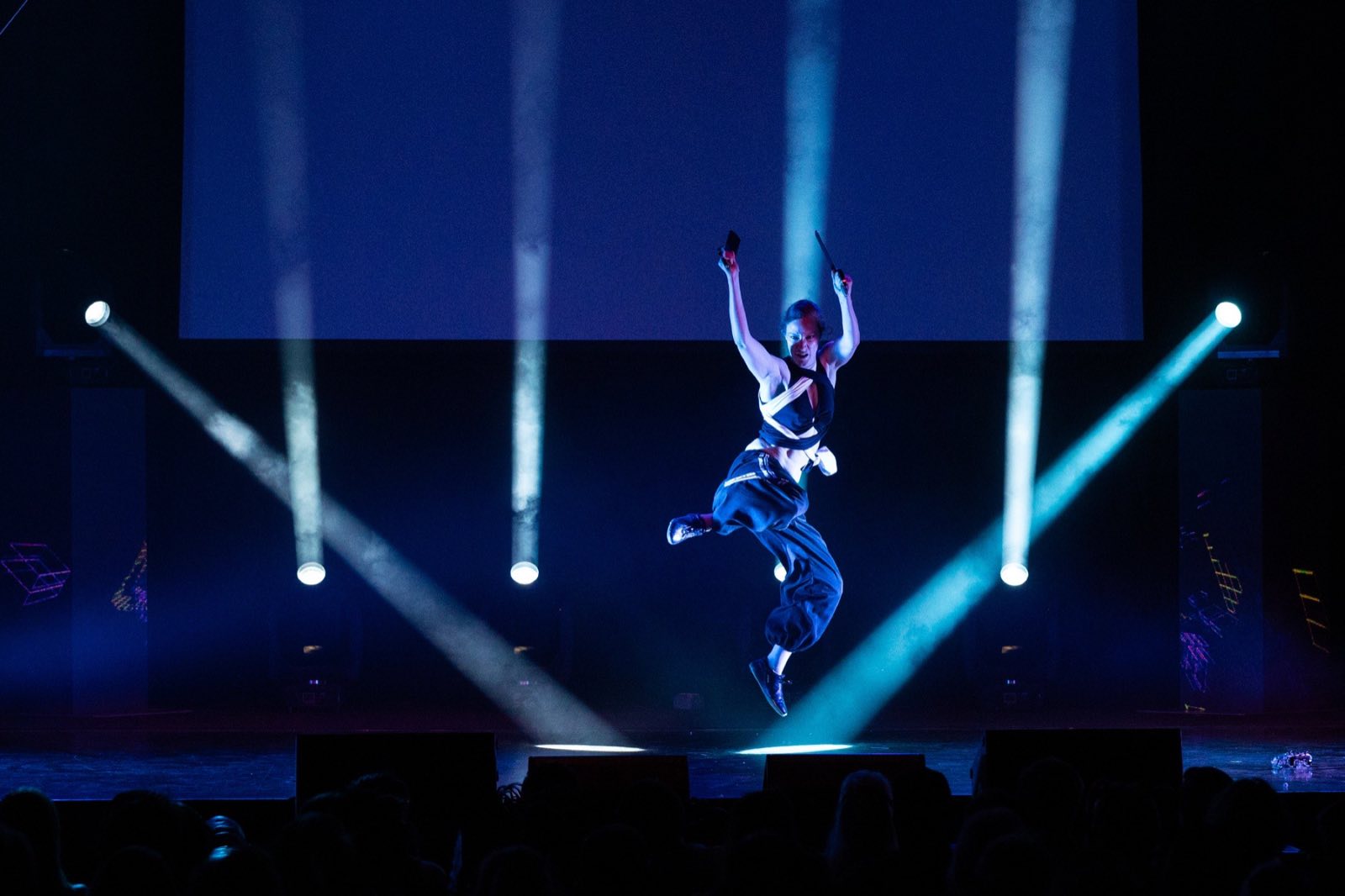 Aerialist suspended high above the stage between white beams of light