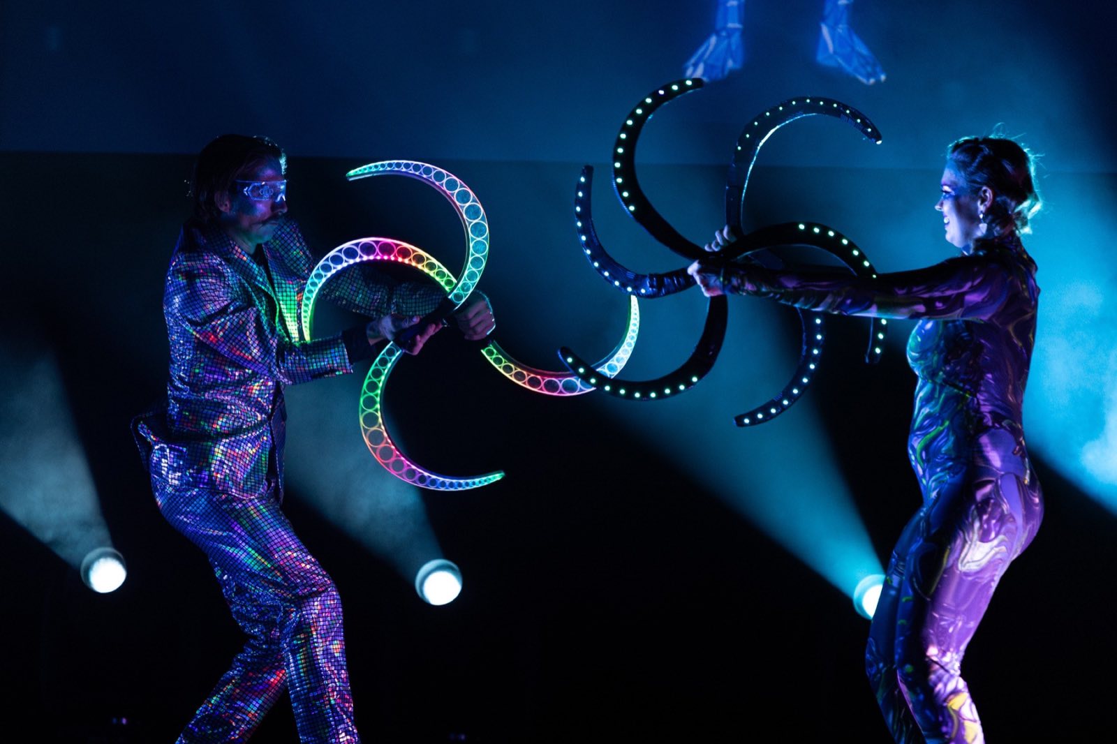 Two metallic-costumed performers interlocking illuminated hoops