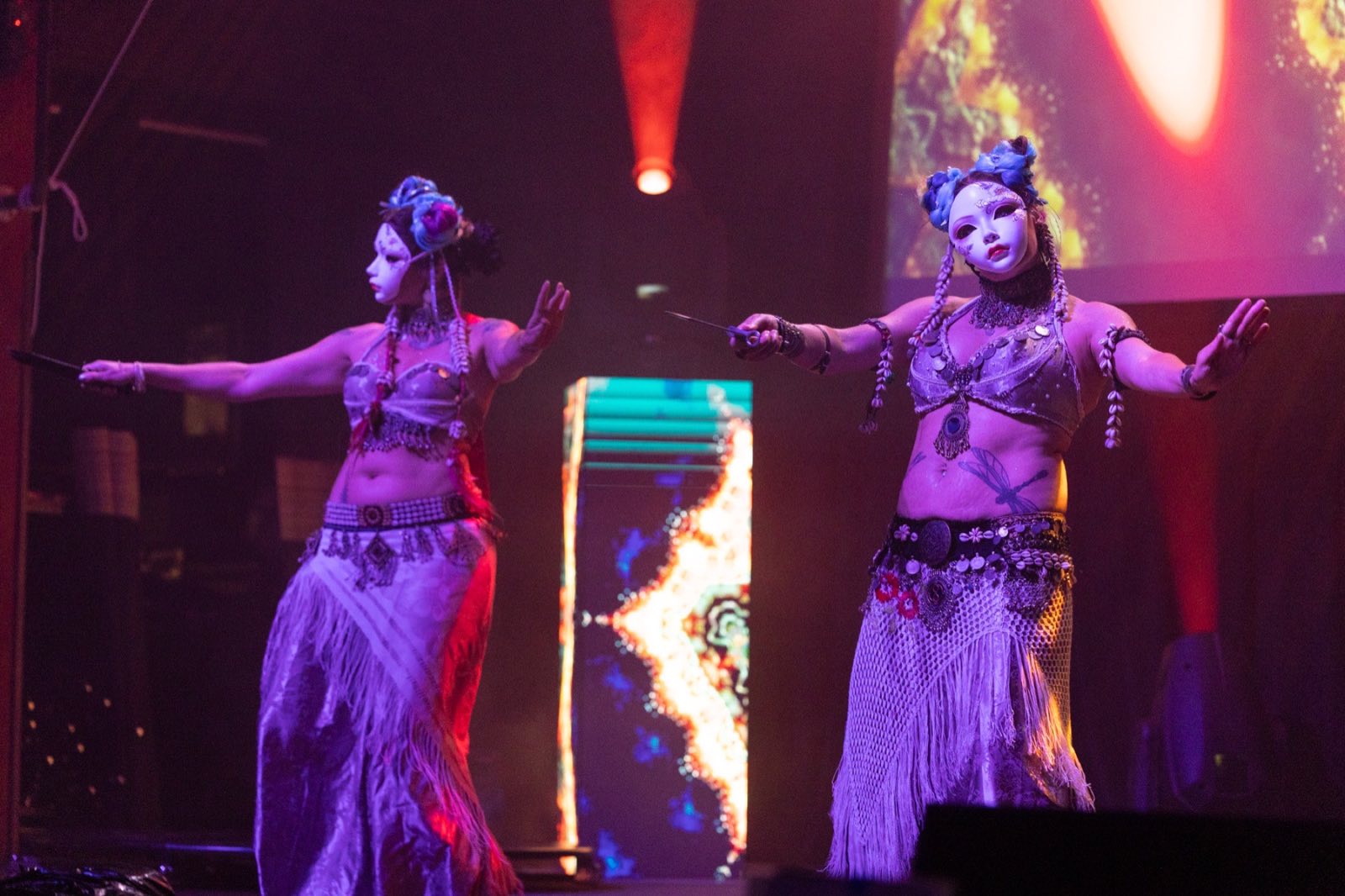 Two dancers extending their arms before fiery projected imagery