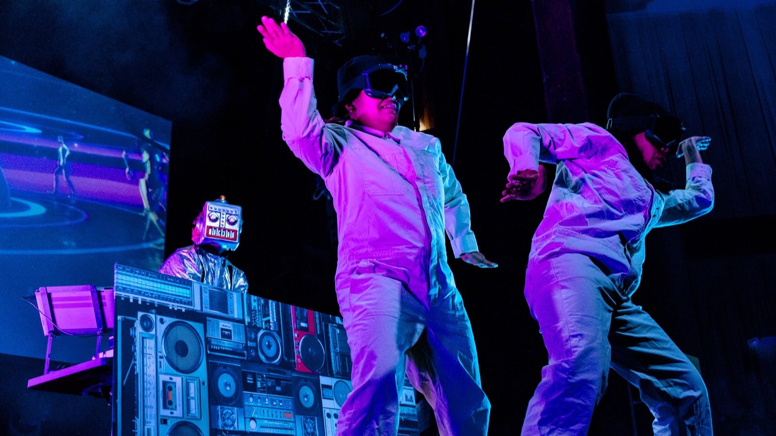 Dancers in white costumes performing before robot scenery