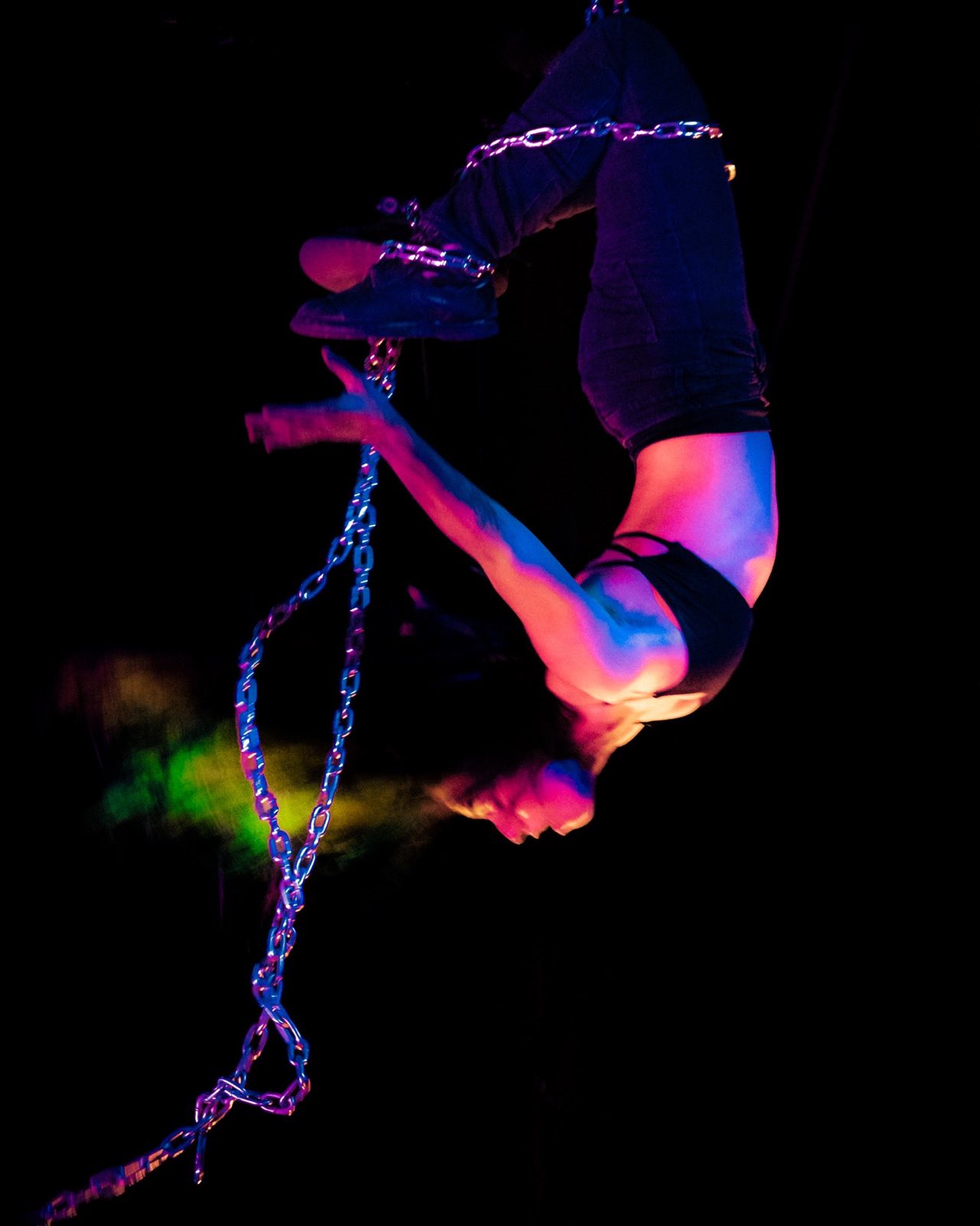 Aerial performer suspended from chains in vivid stage light