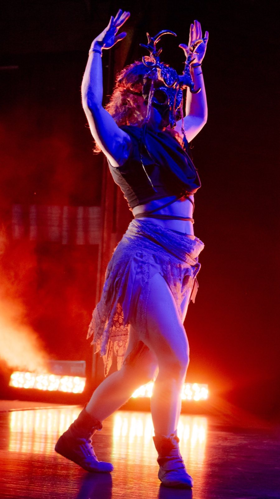 Masked performer moving through red stage light