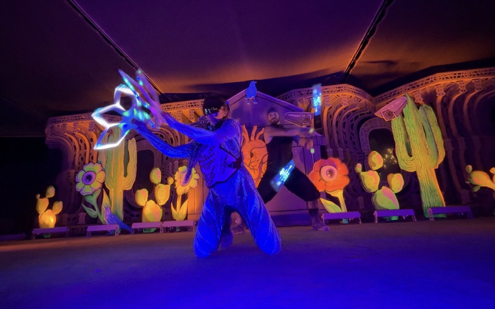 A costumed performer and dancer moving illuminated props across the stage