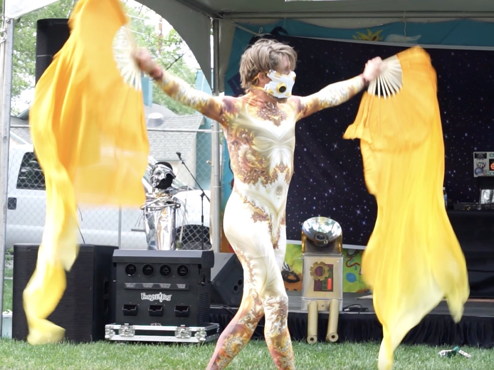 Gold-costumed performer extending two flowing yellow fans onstage