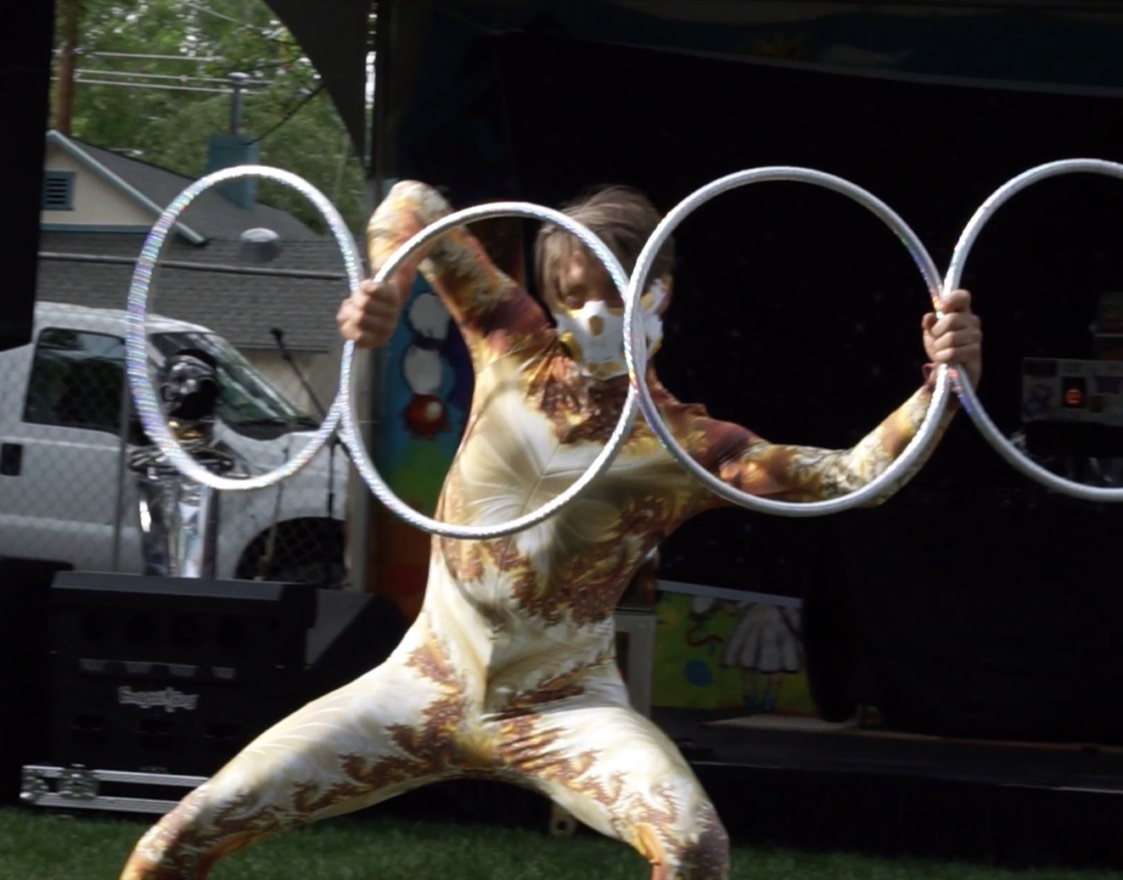 Gold-costumed performer holding three interlocking hoops around her body