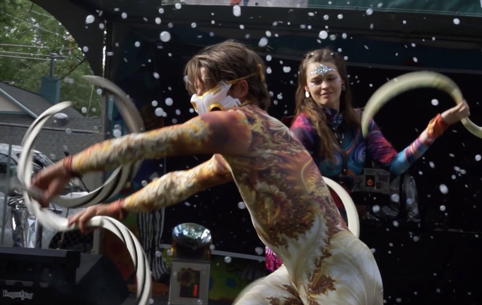 Two costumed performers moving hoops together on the outdoor stage