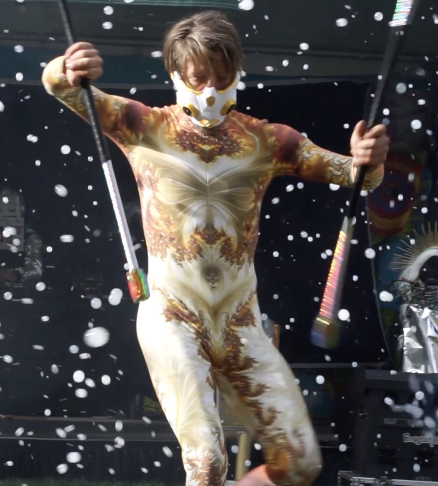 Gold-costumed performer holding two silver hoops beside the bubble-filled stage