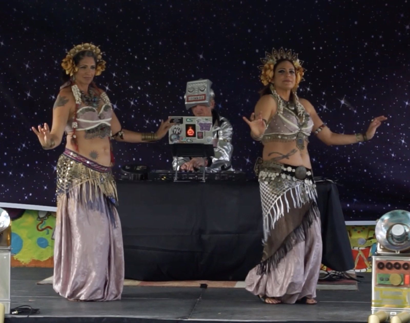 Two silver-costumed dancers performing in front of a handmade robot prop