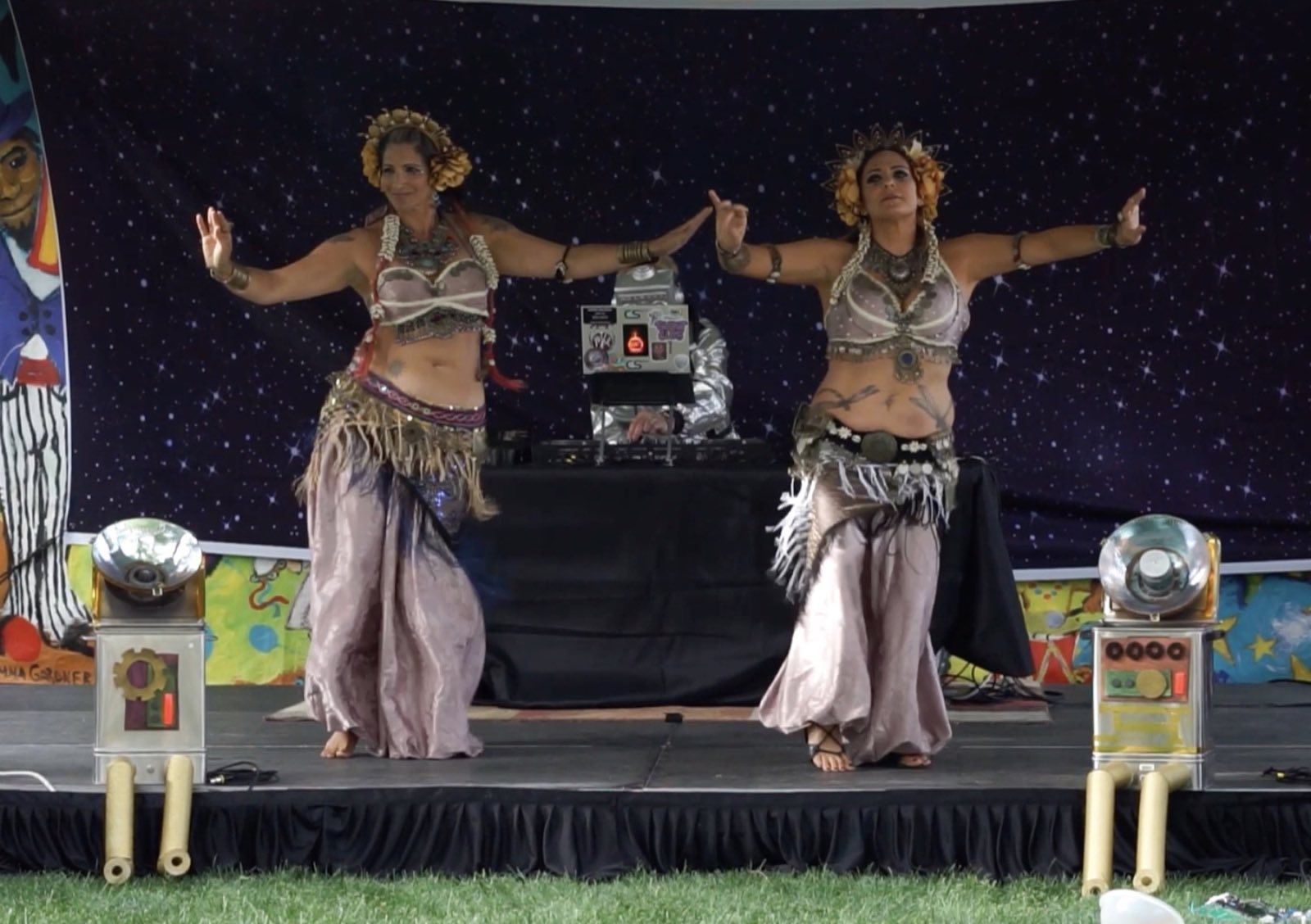Two silver-costumed dancers extending their arms with robot props behind them